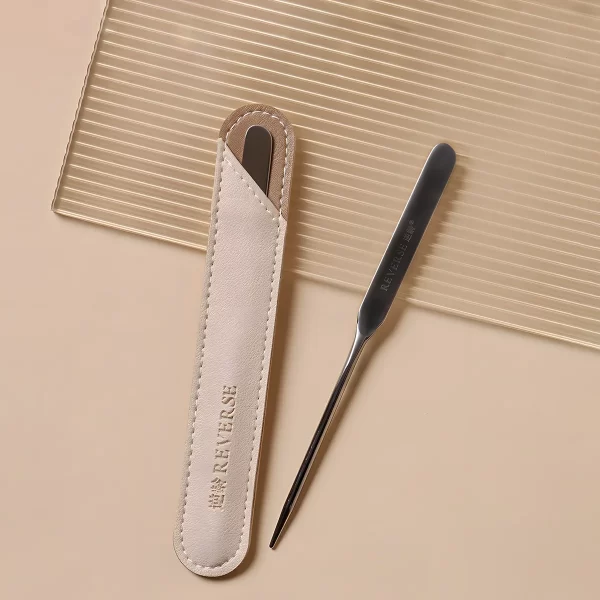 Stainless steel spatula and beige leather case displayed on a textured background.