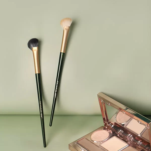 Two fan-shaped nose contour brushes with light and dark bristles next to a contour palette, highlighting their precision and versatility for natural makeup application.